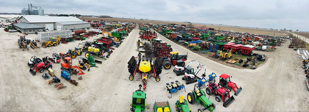 Flygfoto över en lantbruksauktion med rader av traktorer och maskiner.
